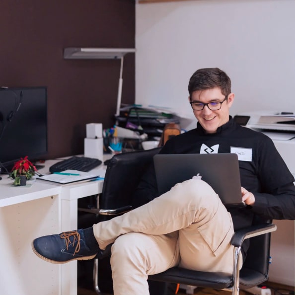 man sitting in a chair looking at his laptop smiling about his website